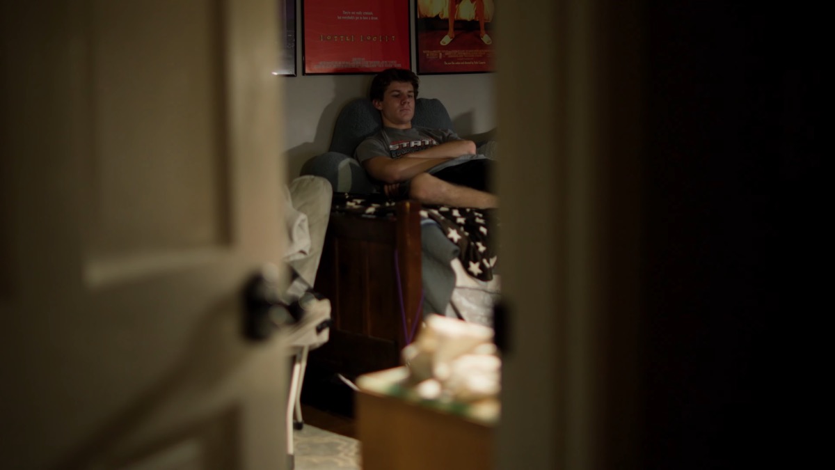 Still from Dead Bent — a figure seen through a partly open door in near darkness.