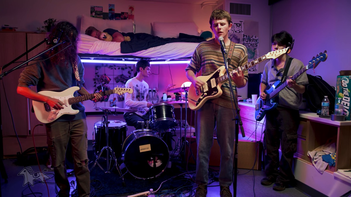 Still from Horsesitter's Tiny Dorm Concert — a four-piece band playing in a dorm room under pink and purple light.