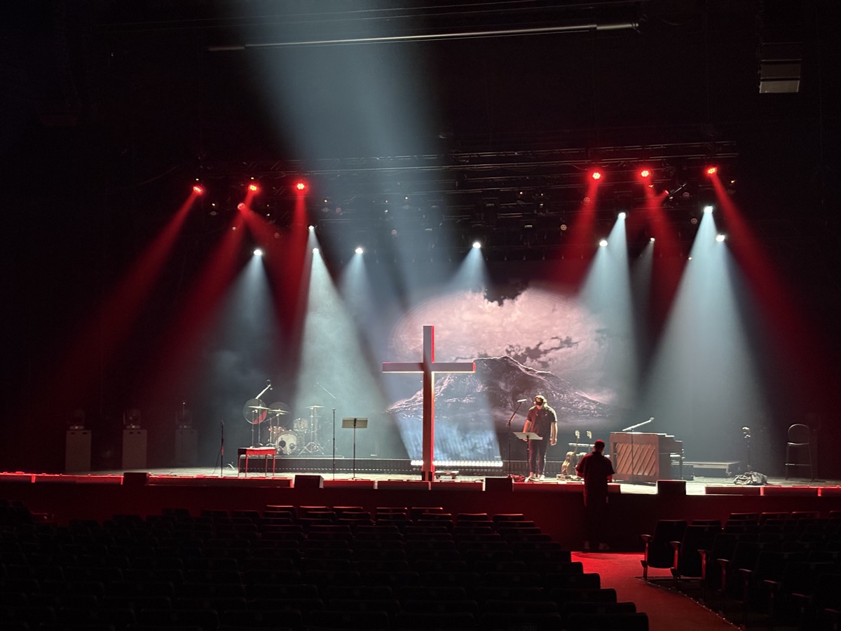 Empty auditorium with red and white beams cutting through haze onto a stage.