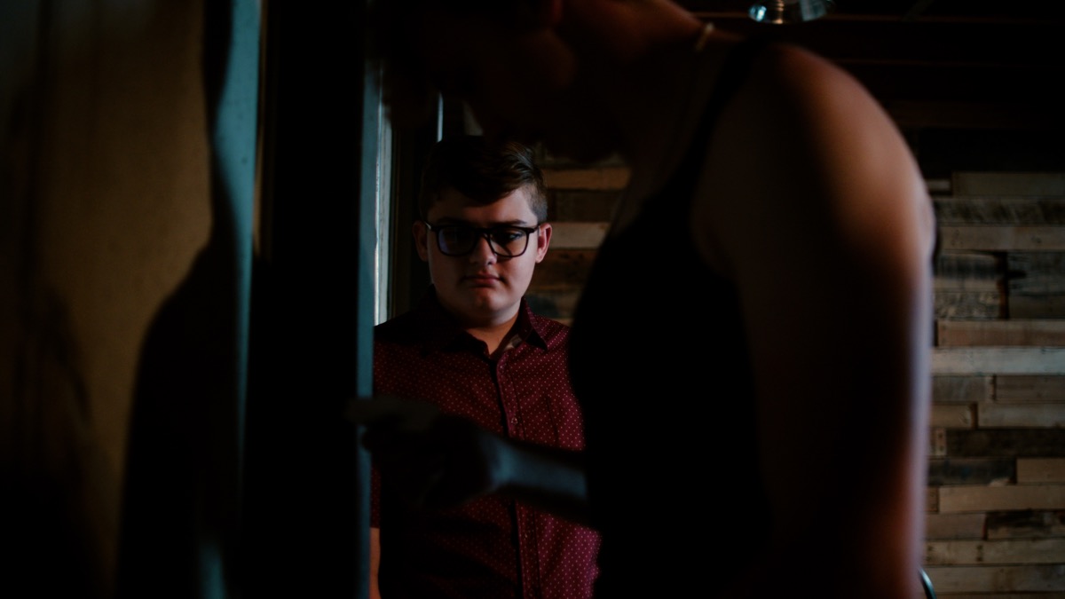 Still from Threshold — a figure lit through a doorway, framed by foreground silhouettes.
